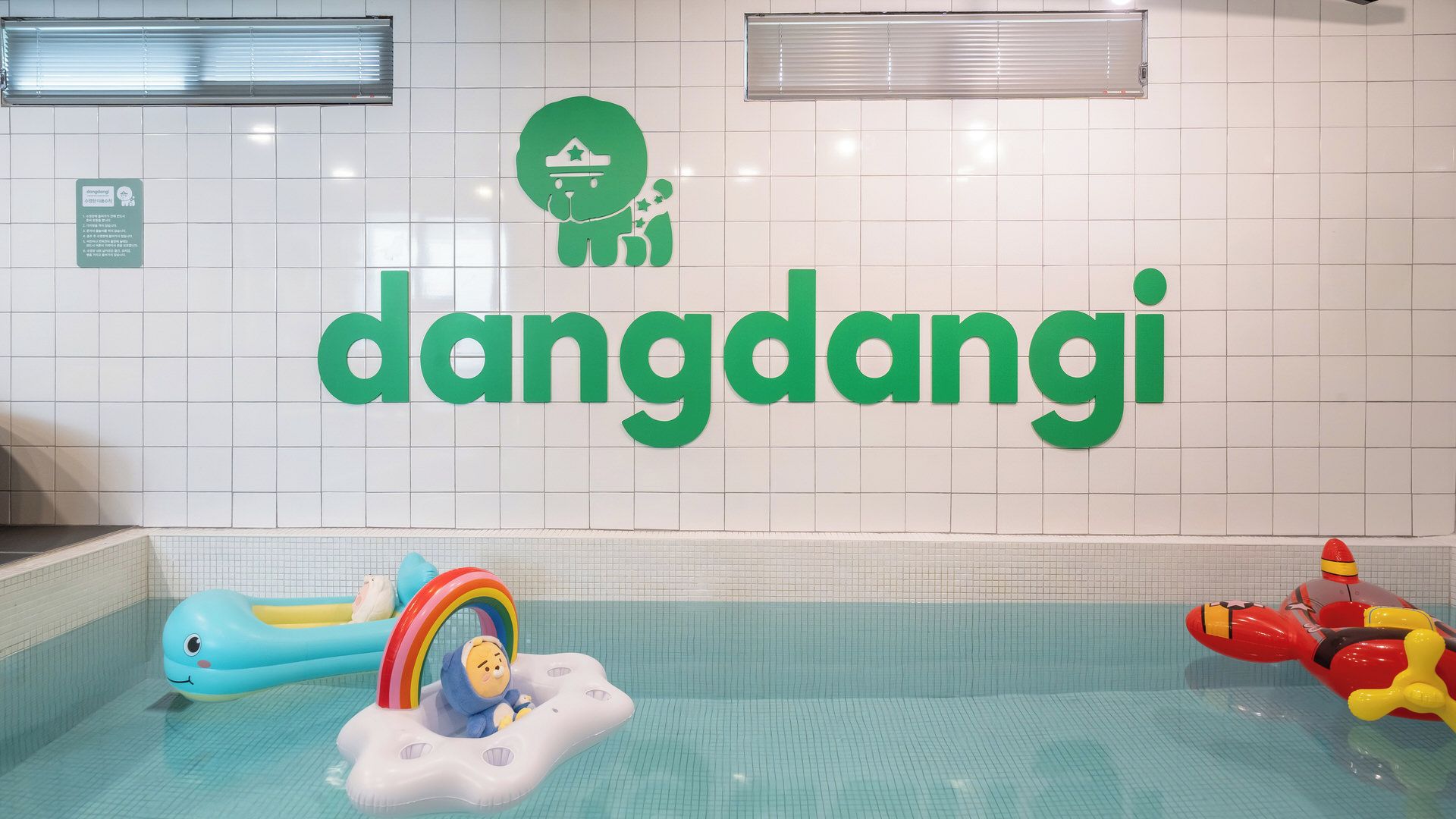 Un área de piscina con un cartel verde grande que dice 'dandangji' y un pequeño juguete inflable con un arcoíris.