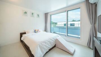 Habitación de hotel con cama, televisor y ventana con vista a un edificio y vegetación.