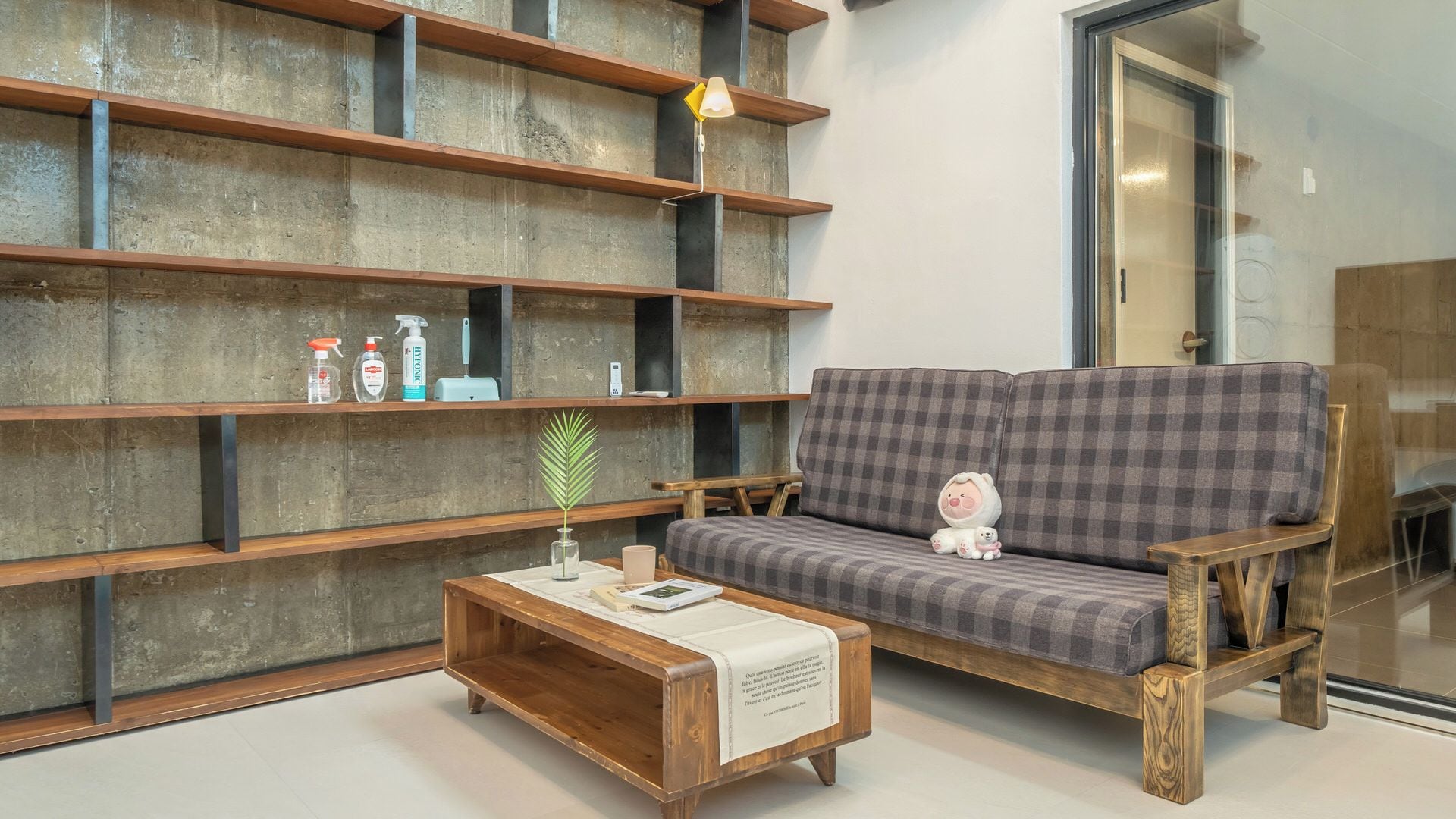 Una sala de estar moderna con un sofá, una mesa de centro de madera y estanterías empotradas frente a una pared de concreto.
