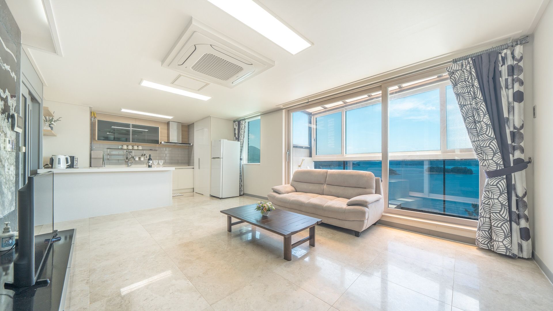Sala de estar moderna com sofá, mesa de centro e vista para o mar através de amplas janelas.