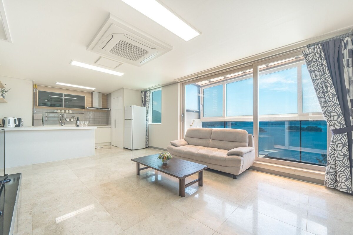 Un salon moderne avec un canapé, une table basse et une vue sur la mer grâce à de grandes fenêtres.