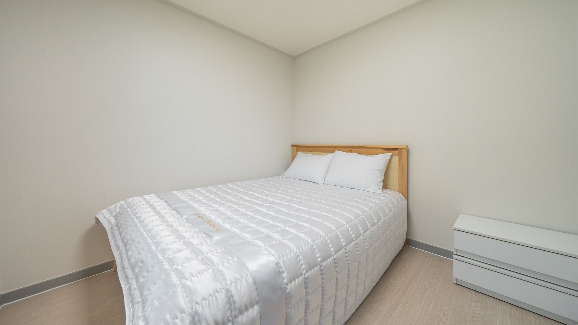 A bedroom with a bed, a wooden headboard, a white bedside table, and a drawer unit.