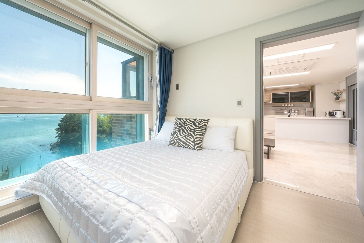 Une chambre avec une grande fenêtre, un lit et une vue sur une étendue d’eau.