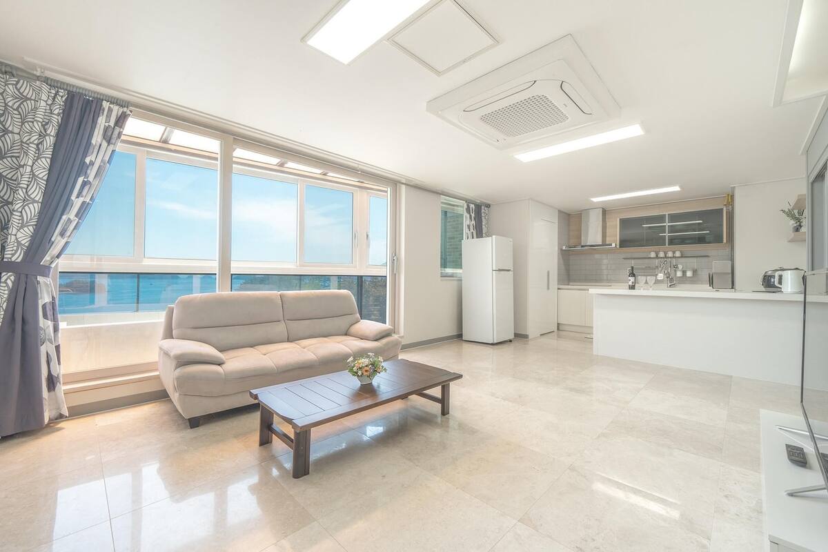 Un apartamento moderno con balcón, sofá, mesa de centro, área de cocina y televisor de pantalla plana.