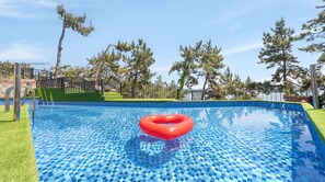 Una piscina con un flotador rojo, rodeada de una valla, árboles y un cielo despejado.