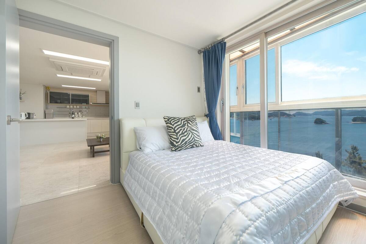 Un dormitorio con una cama grande, vista al mar y una cocina al fondo.