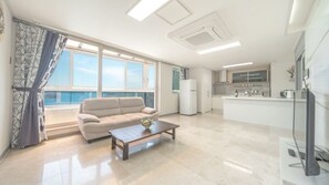 Un salon moderne avec un canapé, une table basse et une vue sur la mer grâce à de grandes fenêtres.