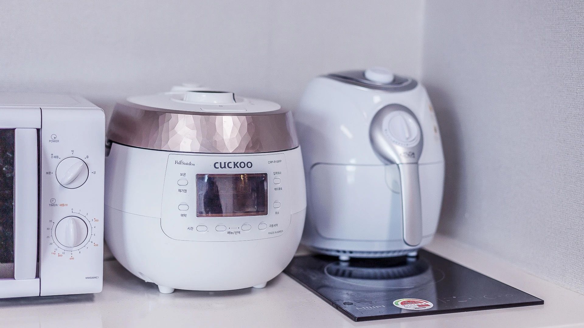 Three kitchen appliances: a microwave, a rice cooker, and a coffee maker.