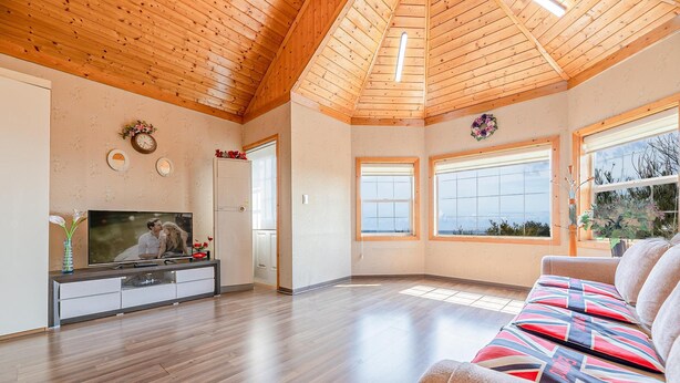 A spacious living room with a wooden ceiling, large windows, a flat-screen TV, and a sofa with patterned cushions. - Ganghwa Western Beach Pension (Incheon)