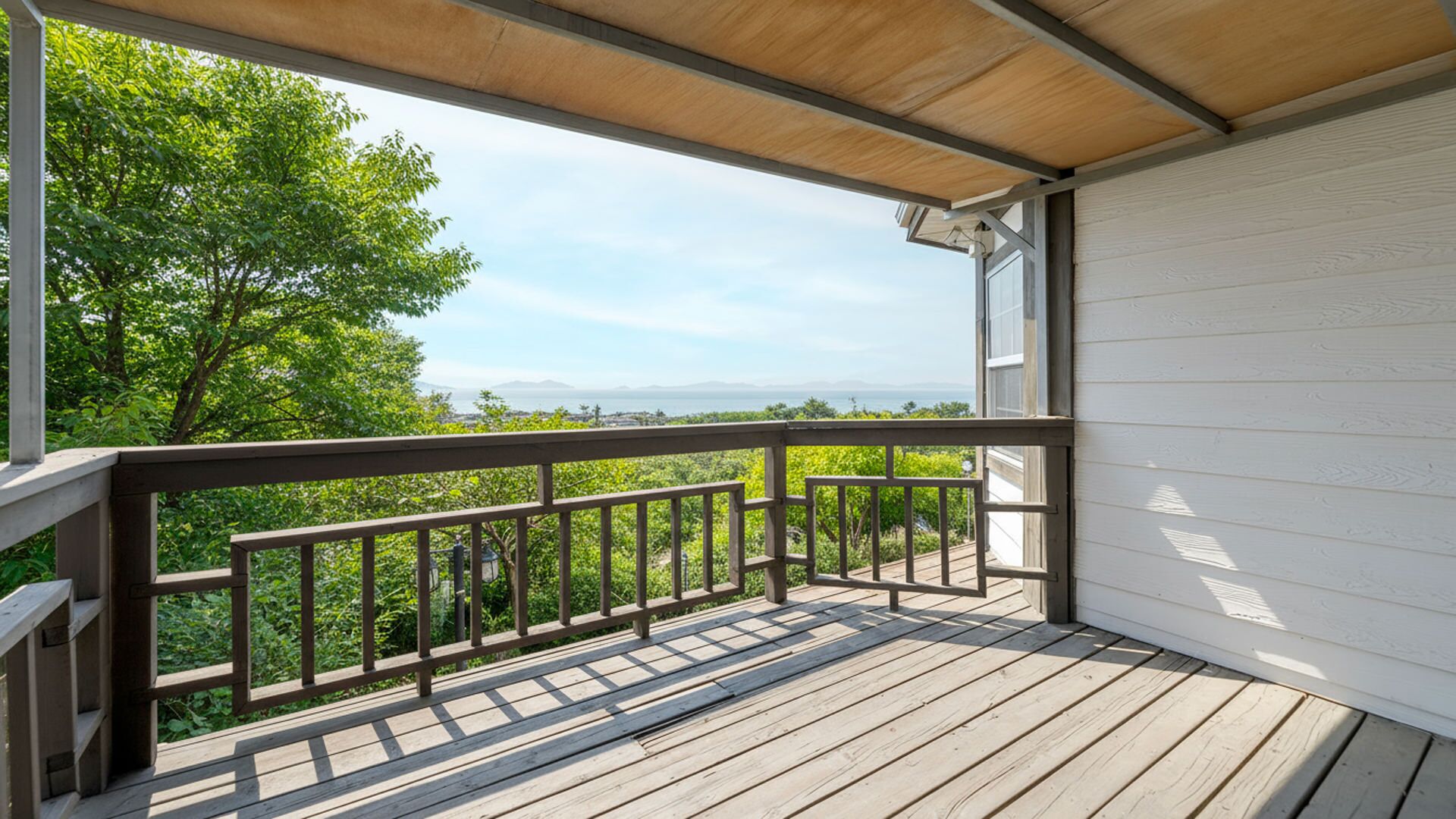 A wooden deck with a railing, overlooking a lush green landscape and a distant view of the ocean.