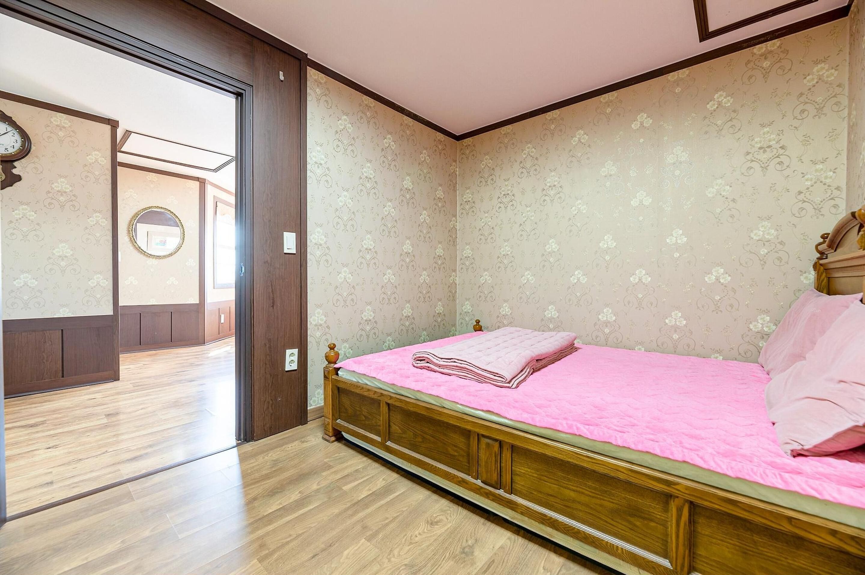Un dormitorio con una cama de madera, una colcha rosa y papel tapiz floral.