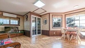 A living room with a wooden floor, a television, a dining table with chairs, and a large window. - Ganghwa Western Beach Pension (Incheon)