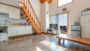 A spacious living area with a wooden staircase, a kitchen with white cabinets, a dining table, and a large window providing a view of the outdoors. - Ganghwa Western Beach Pension (Incheon)
