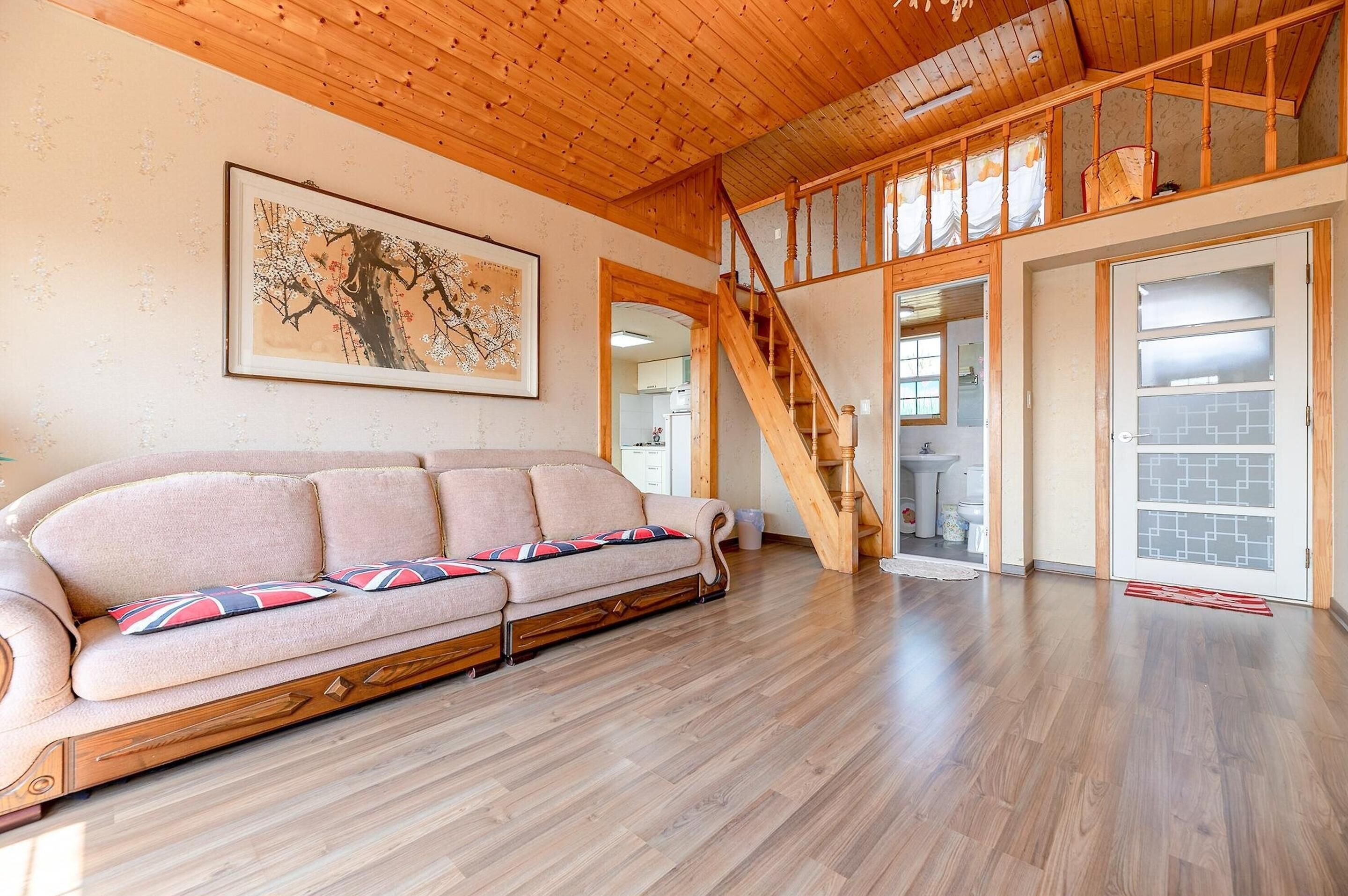 Un salón amplio con techo de madera, un sofá con cojines estampados y una escalera que sube a un nivel superior.