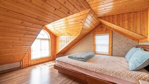 A bedroom with a sloped ceiling, wooden walls, a bed with a quilted cover, and two windows. - Ganghwa Western Beach Pension (Incheon)