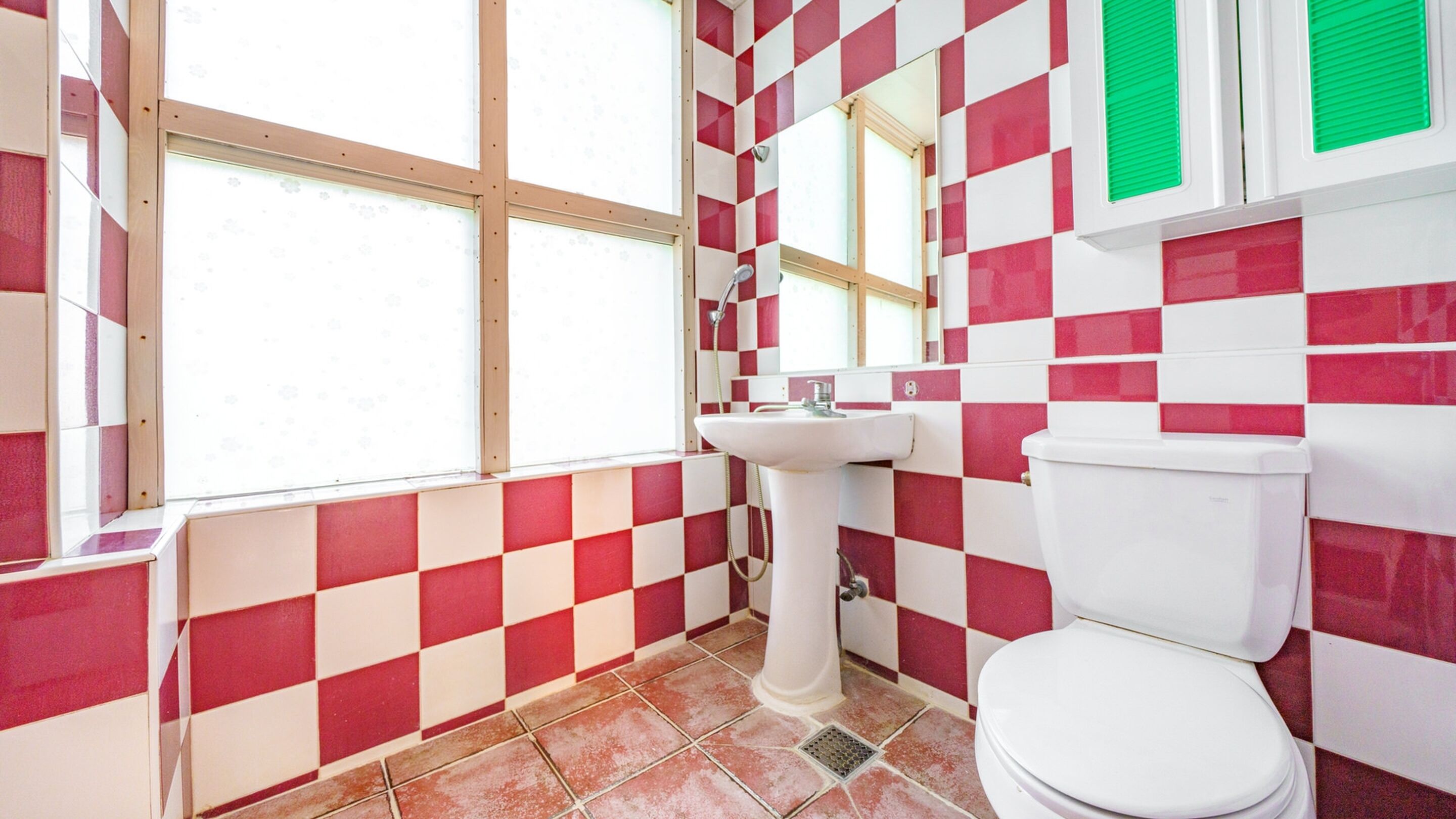 Een badkamer met rode en witte geruitelde tegels, een witte wastafel en een toilet.