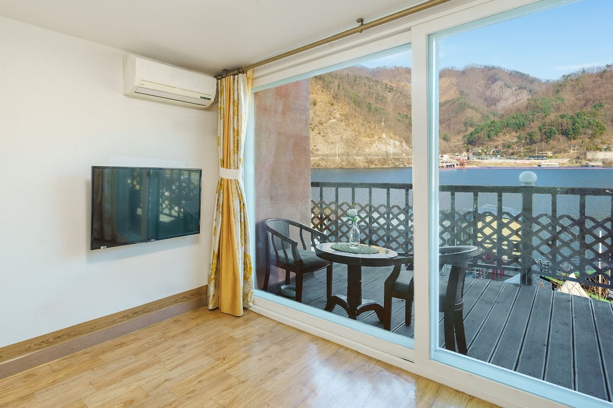 Un balcon avec une table et des chaises, un téléviseur fixé au mur et une vue sur un lac et des montagnes.