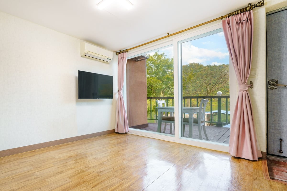 Une pièce spacieuse dotée d’un plancher en bois, d’un téléviseur à écran plat fixé au mur et d’une porte-fenêtre coulissante donnant sur un espace extérieur aménagé avec une table et des chaises.