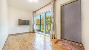 Ein geräumiges Zimmer mit Holzboden, einer Schiebetür zu einem Außenbereich und einem an der Wand befestigten Fernseher.