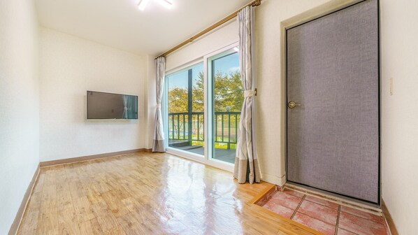 A spacious room with a wooden floor, a sliding glass door leading to an outdoor area, and a mounted television on the wall. - Gapyeong Elin Pension (Gapyeong)