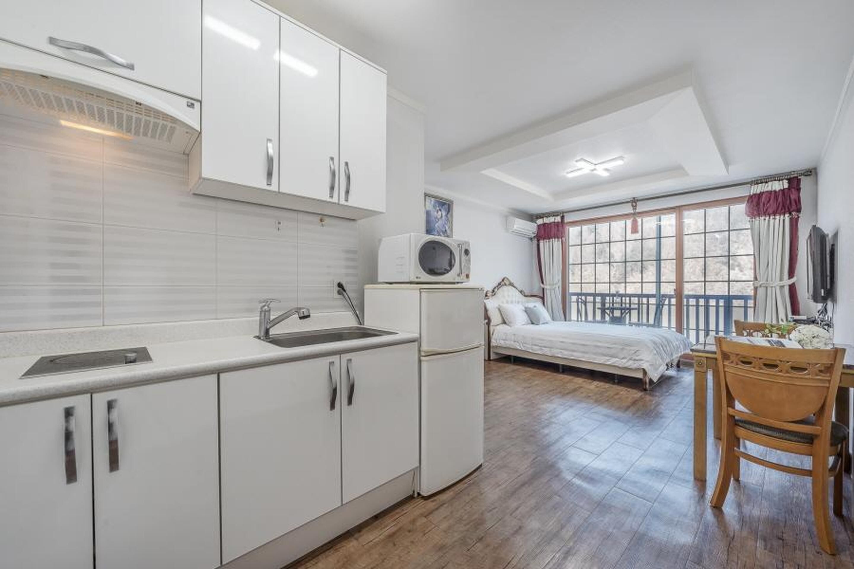 A compact room with a kitchenette, a bed, and a window with curtains.