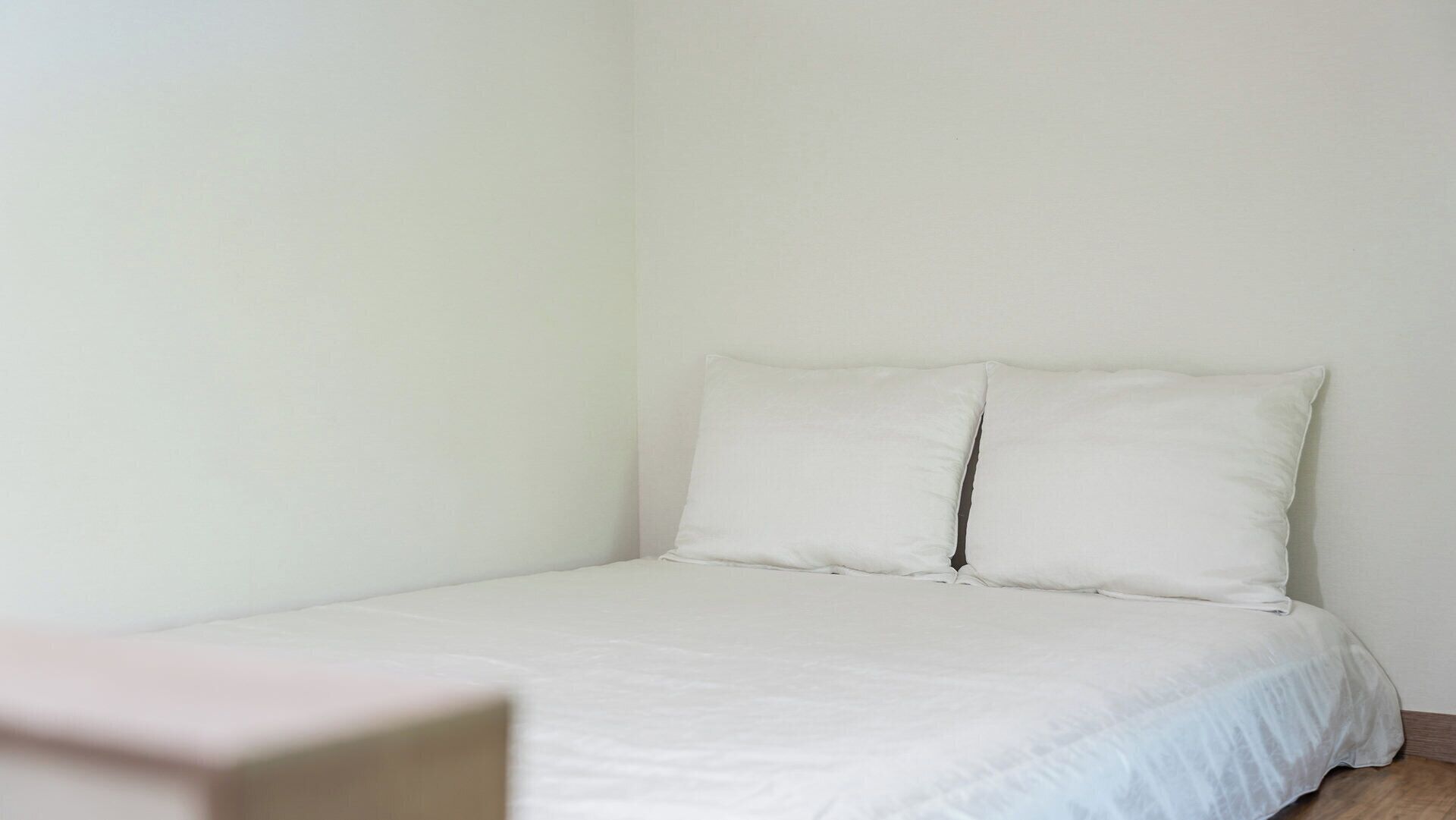 Un dormitorio sencillo y sin adornos con una cama individual, ropa de cama blanca y suelo de madera.