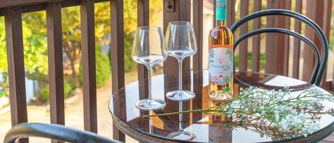 Una mesa de cristal con una botella de vino Mouton Cadet, dos copas de vino vacías y una rama con flores blancas en un balcón.
