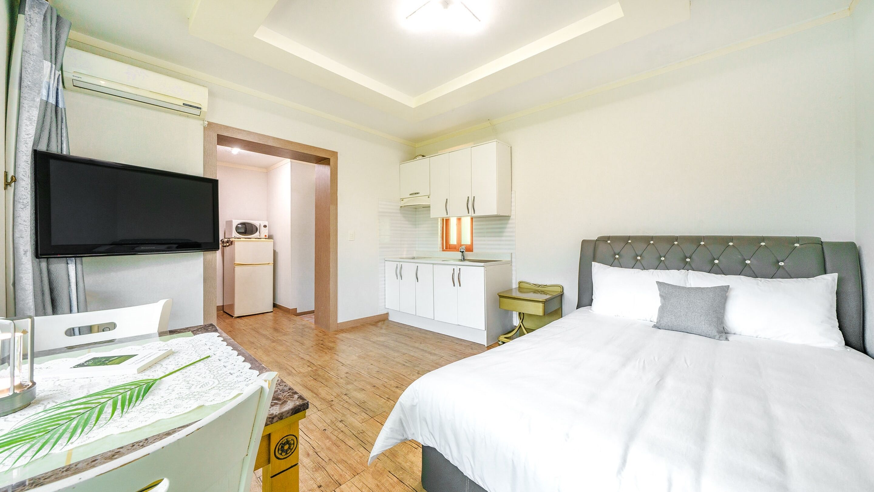 A bedroom with a bed, a television, a small kitchenette, and a bathroom.