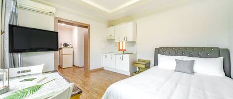 A bedroom with a bed, a television, a small kitchenette, and a bathroom.