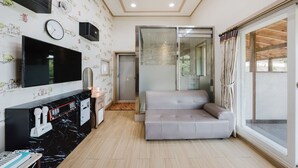 A modern living room with a sofa, a flat-screen TV, a fireplace, and a glass shower enclosure. - Gapyeong Art Pension (Gapyeong)