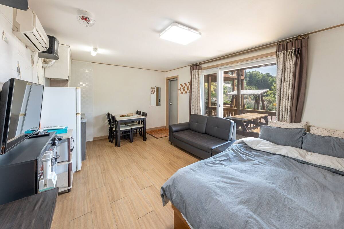 A compact hotel room with a bed, a sofa, a small dining table, and a kitchenette.