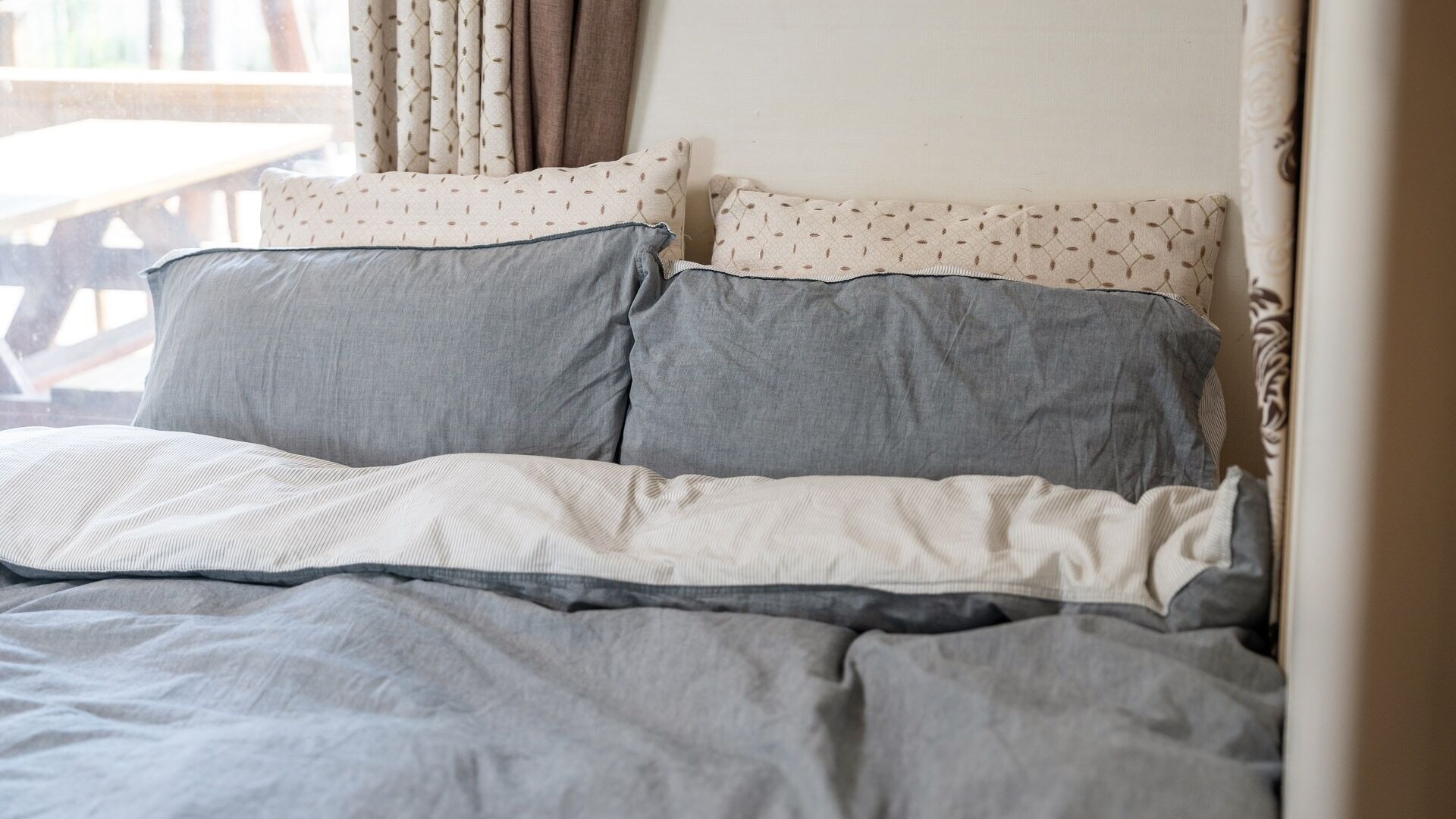 A bed with grey bedding and patterned pillows.