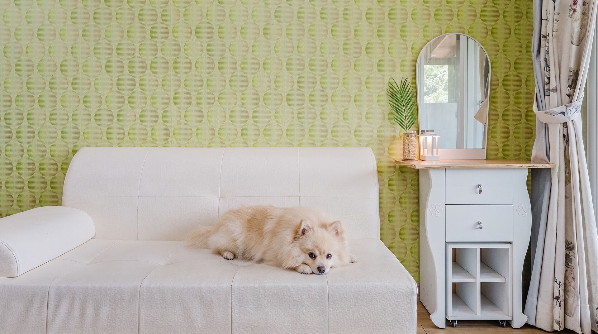 Ein Zimmer mit einem weißen Sofa, einem kleinen weißen Schrank und einem Spiegel.