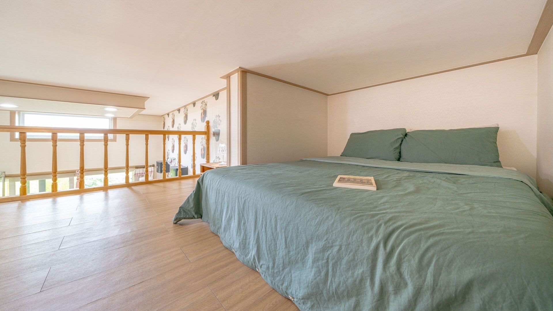A bedroom with a large bed, a wooden floor, a balcony with a railing, and a view of the outdoors.