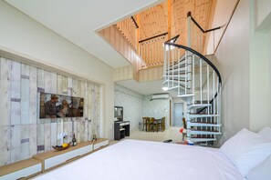 A bedroom with a spiral staircase, a TV mounted on the wall, a dining area, and a bed with white linens. - Gangneung 2block Pension (Gangneung)