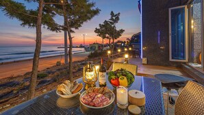 Une table dressée avec de la nourriture et des boissons sur un balcon donnant sur la plage au coucher du soleil.