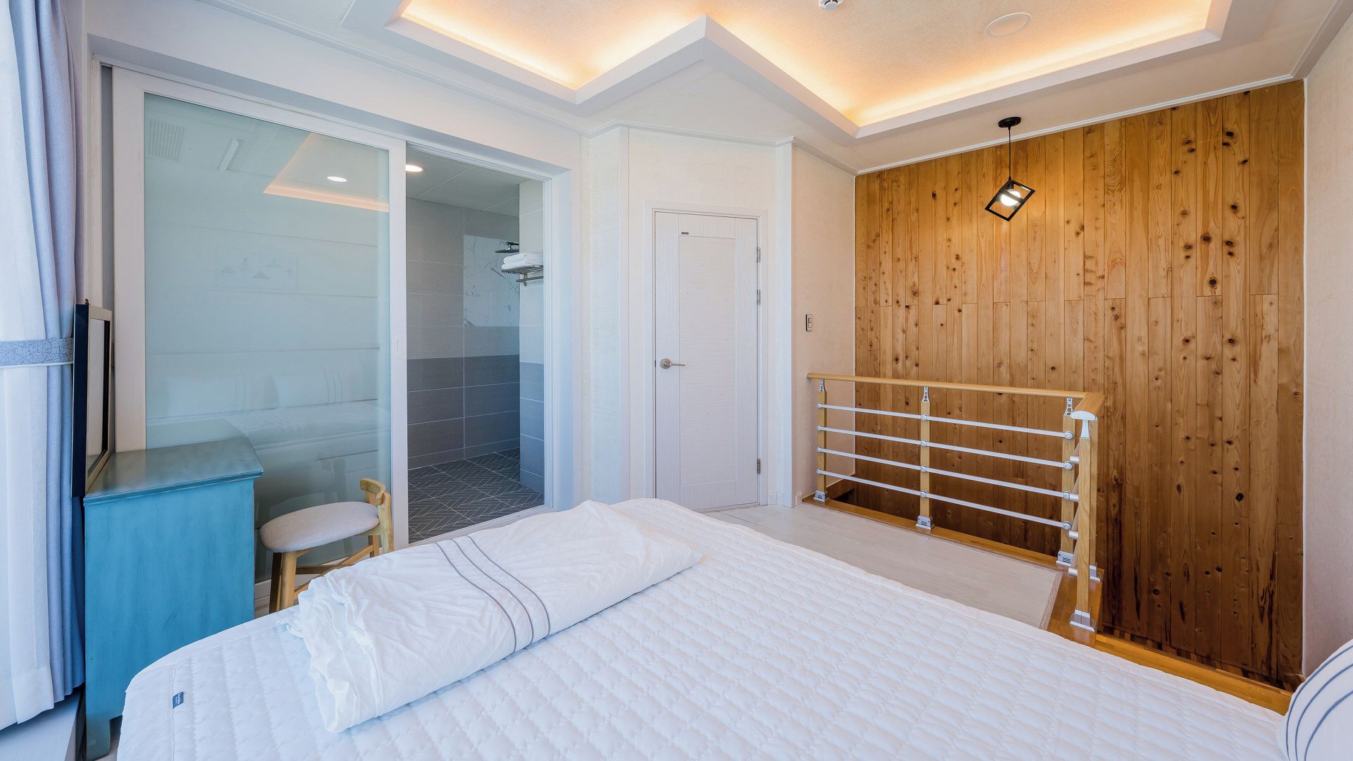 Un dormitorio moderno con una cama, un armario de madera, una cabina de ducha de vidrio y una mesita de noche azul.