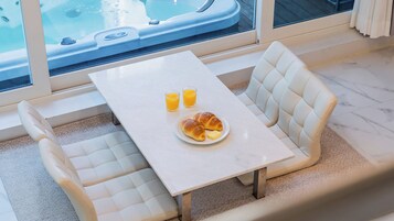 Un comedor con mesa y sillas, un jacuzzi al fondo y una disposición para desayuno con cruasanes y jugo de naranja.