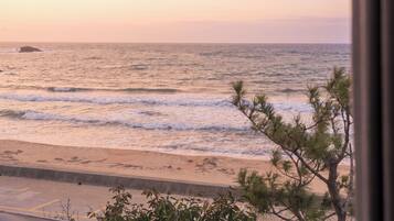 A beach view with waves, a sandy shore, and a tree in the foreground.