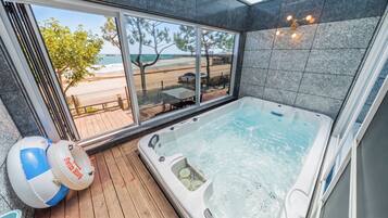 A modern bathroom with a large bathtub, a view of the beach, and a wooden deck outside.