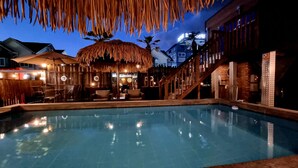 A swimming pool with a thatched roof seating area, wooden fence, and a staircase leading to an upper level. - Gyeongju Suite Cream Hill Pension (Gyeongju)