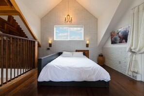 Une chambre Ă coucher avec un lit, une fenĂȘtre, un lustre, un tableau au mur et un escalier.