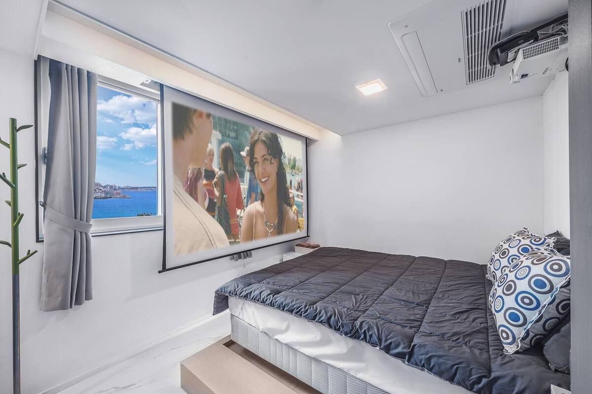 A bedroom with a bed, a TV mounted on the wall, and a window with curtains.