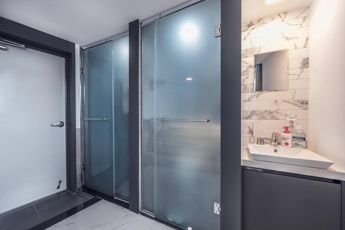 A modern bathroom with a glass shower enclosure, a marble-tiled wall, and a sink with toiletries.