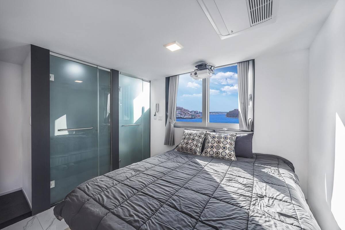 A modern bedroom with a large bed, a sliding door closet, and a view of the sea.