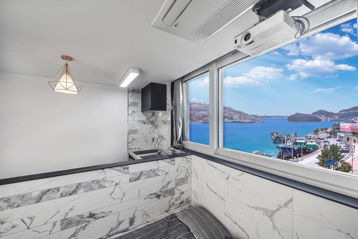 A bathroom with a view of a coastal town, marble tiles, a hanging light fixture, and a built-in speaker.