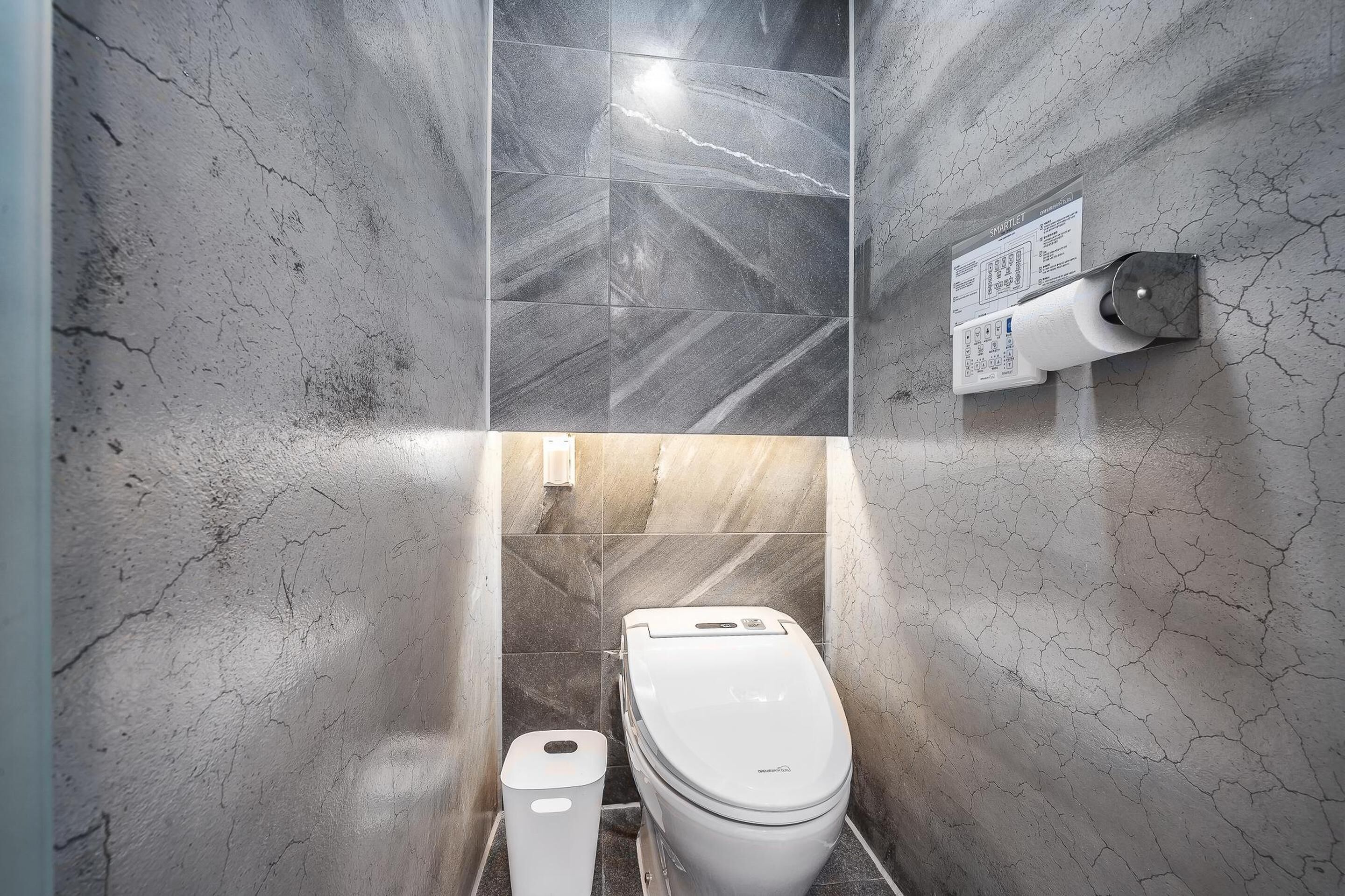 Un baño con inodoro y bidé, paredes con azulejos y dispensador de toallas de papel adherido a la pared.