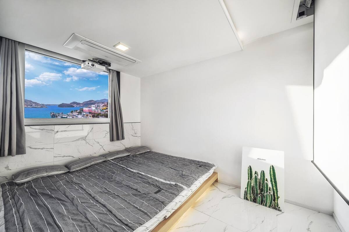 A bedroom with a bed, a window with curtains, a projector, and a cactus artwork.