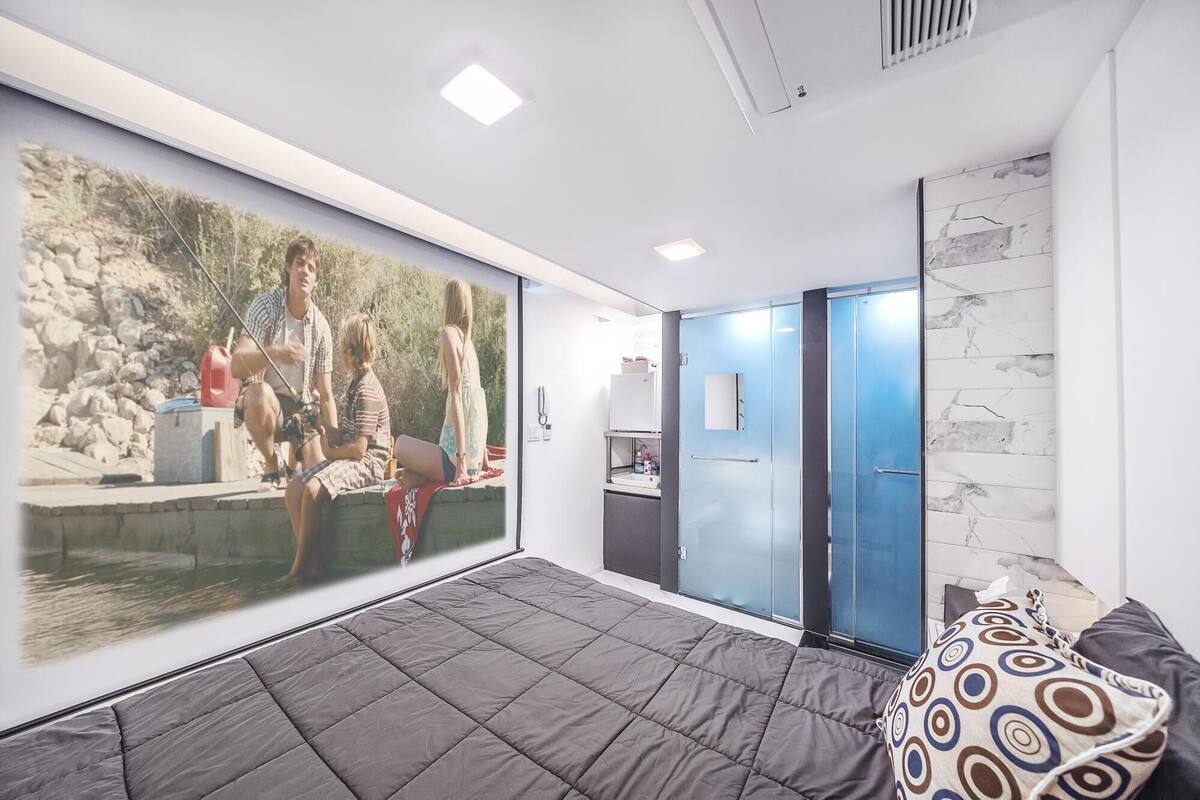A modern room with a large bed, a wall-mounted TV, a blue door, and a marble-patterned wall.