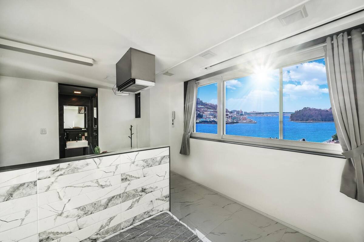 A modern hotel room with a large window offering a view of a coastal city.